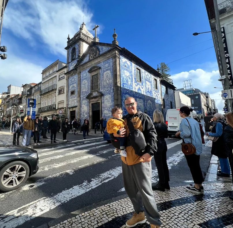 Leo com o Álvaro no colo em frente a uma igreja coberta de azulejos, no Porto